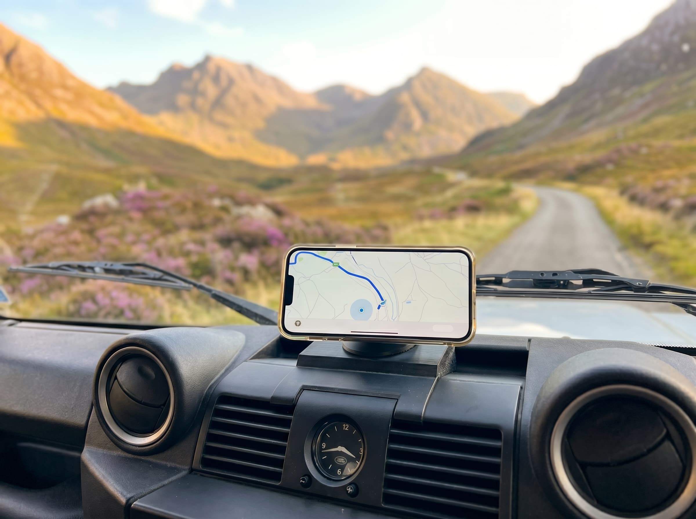 Magnotex3D MagSafe dash mount holding a phone on a Land Rover Defender, mountain pass beyond the windscreen